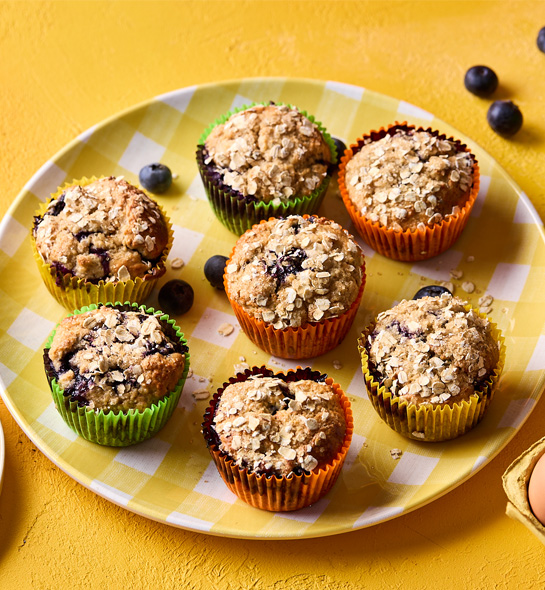 Seven blueberry and oat breakfast muffins sit on a yellow and white checkered plate